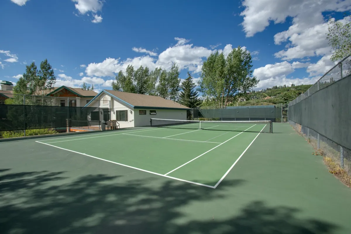 An outdoor tennis court surrounded by trees and adjacent to a building, capturing a lively, social vibe perfect for active recreation and friendly competition.