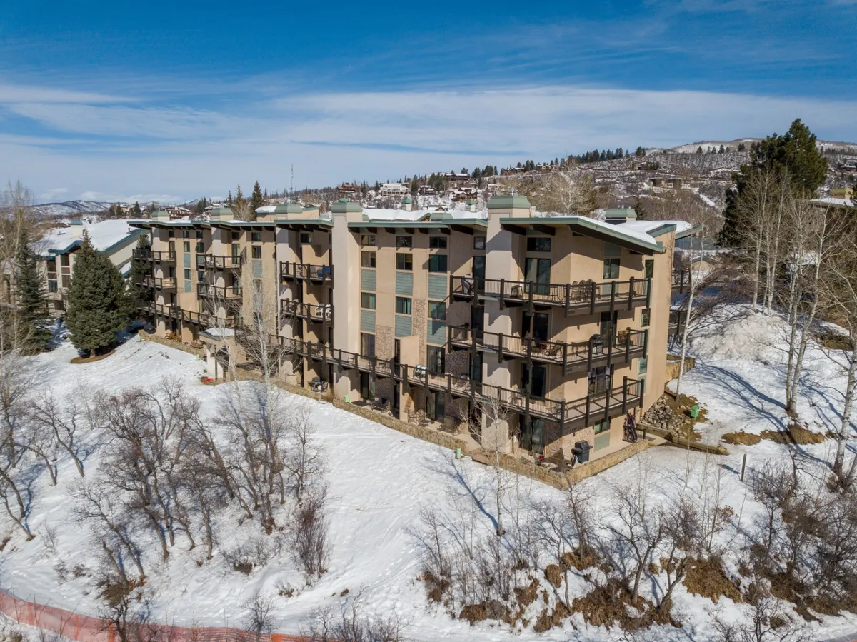 A multi-story building is shown with balconies facing a snow-covered landscape. Trees surround the building, and each balcony has a vantage point for enjoying the peaceful mountain setting. The wintry atmosphere underlines the tranquility and connection to nature offered from each private perch.