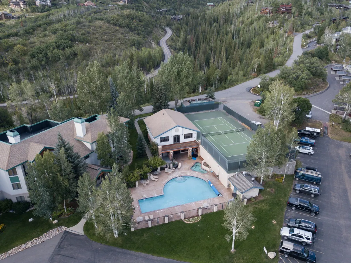 The image showcases the inviting exterior of Storm Meadows Club, featuring a sparkling heated swimming pool surrounded by a landscaped garden, a well-maintained tennis court, and ample space for outdoor gatherings. The leisure amenities are bathed in warm light, suggesting a relaxing and active mountain getaway.