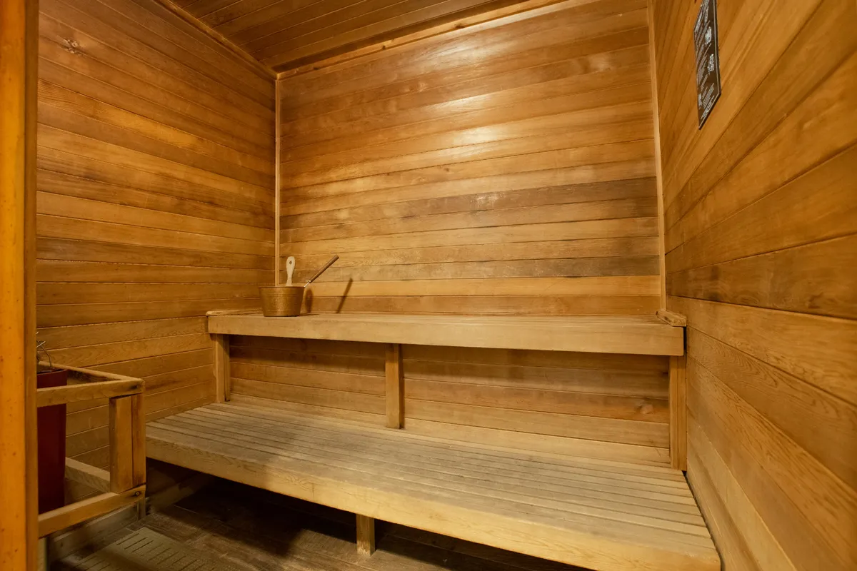 A serene interior sauna space with wooden benches, walls, and a bucket and ladle, suggesting a tranquil environment for relaxation and self-care.