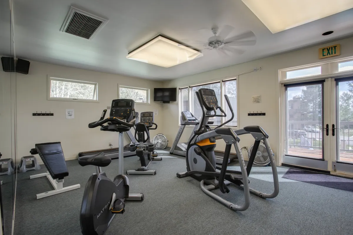 A well-equipped fitness center with treadmills, elliptical machines, an exercise bike, free weights, and a mirrored wall. The space is bright, energetic, and ready for personal workouts or group fitness sessions.