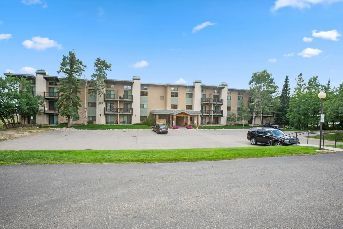 This image shows the exterior facade of a building in the Storm Meadows Club development, with its entrance area, parking lot, and mature trees creating a welcoming and accessible first impression. The perspective highlights the proximity of neighboring units and the communal nature of the property.
