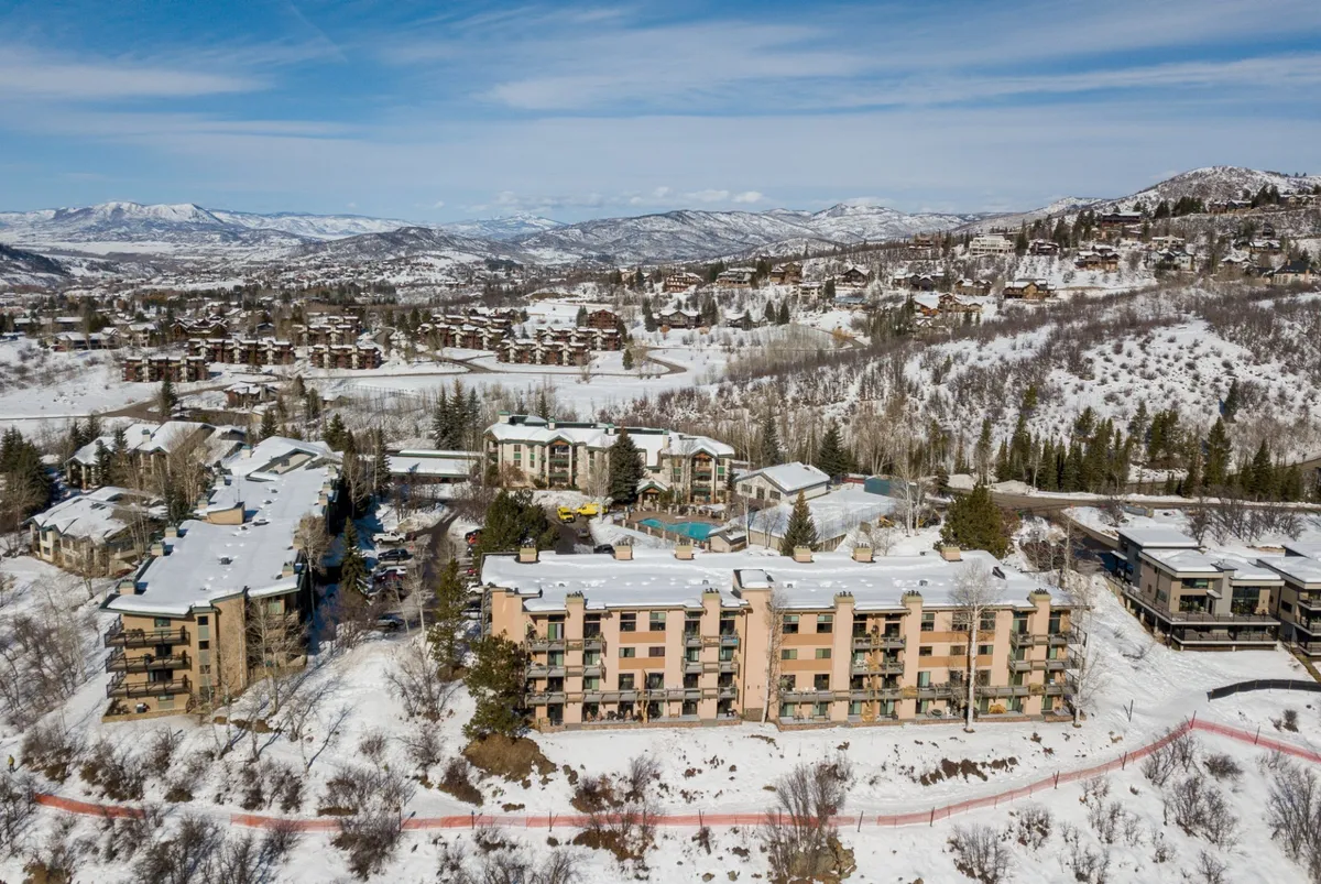 An inviting winter scene of snow-covered buildings and mountains, with a glimpse of the swimming pool area nestled among trees. The area exudes a sense of relaxation after outdoor activities, hinting at resort amenities for families returning from the slopes.