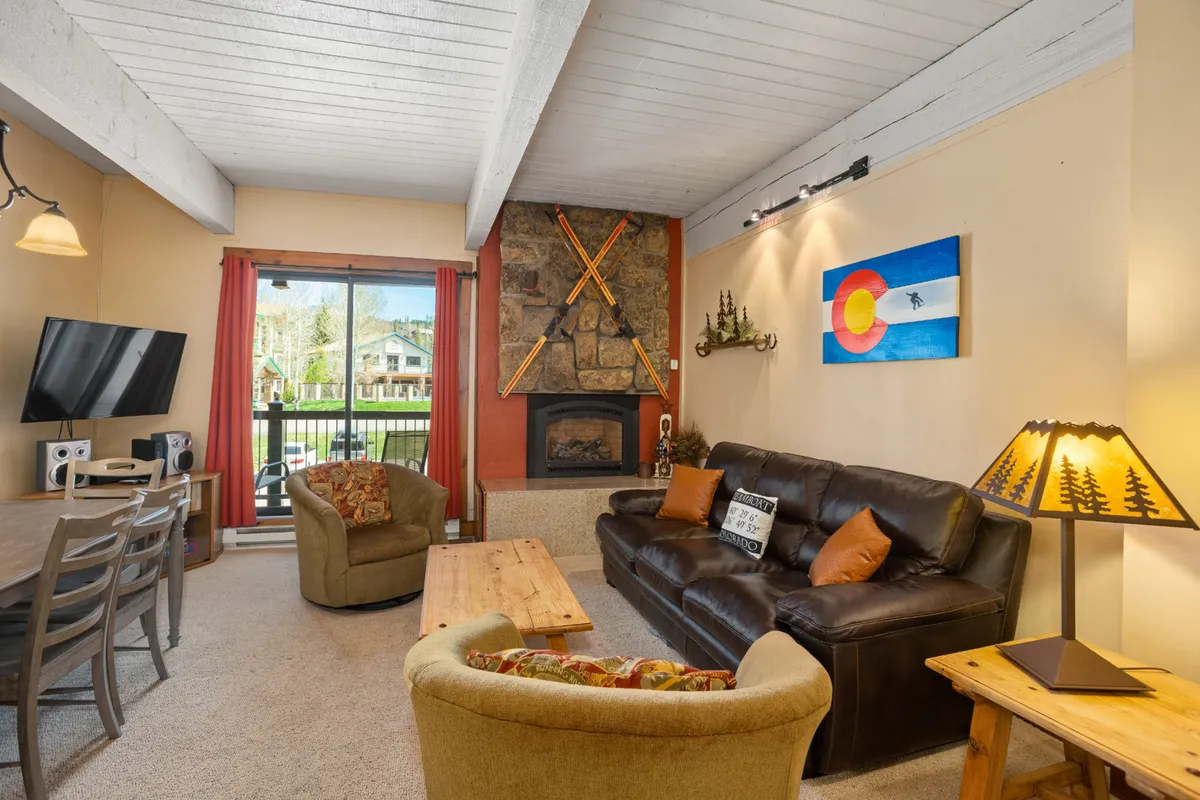 A cozy interior space featuring a glowing fireplace, comfortable sofa, dining table, and tasteful wall art. Large windows hint at mountain views, while the atmosphere feels peaceful and inviting—perfect for relaxing mornings or winding down together.
