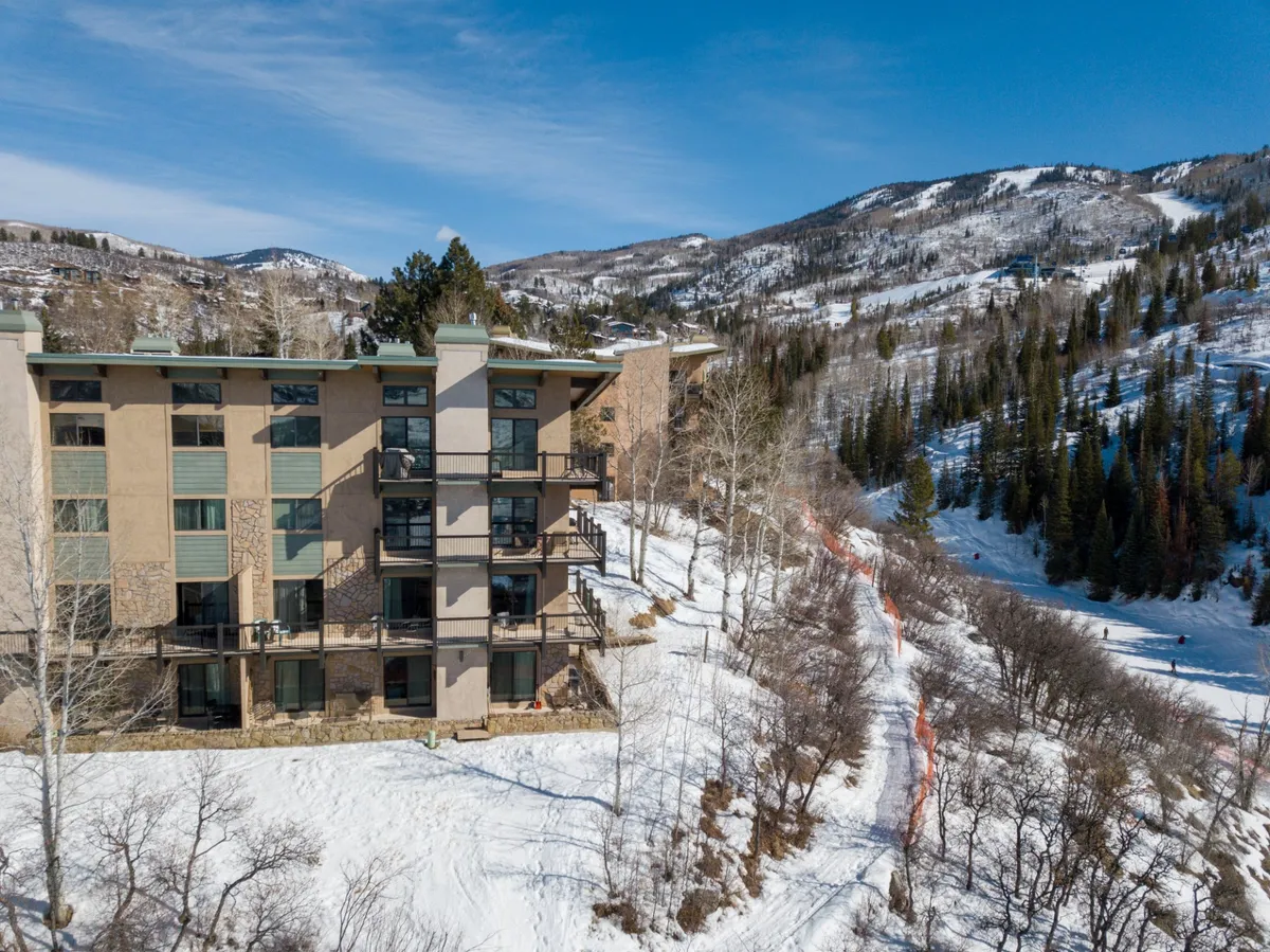 A wide shot of an apartment building surrounded by a snow-covered landscape, framed by trees and a majestic mountain backdrop. The image evokes the peaceful and picturesque setting where several similar units can be booked together.