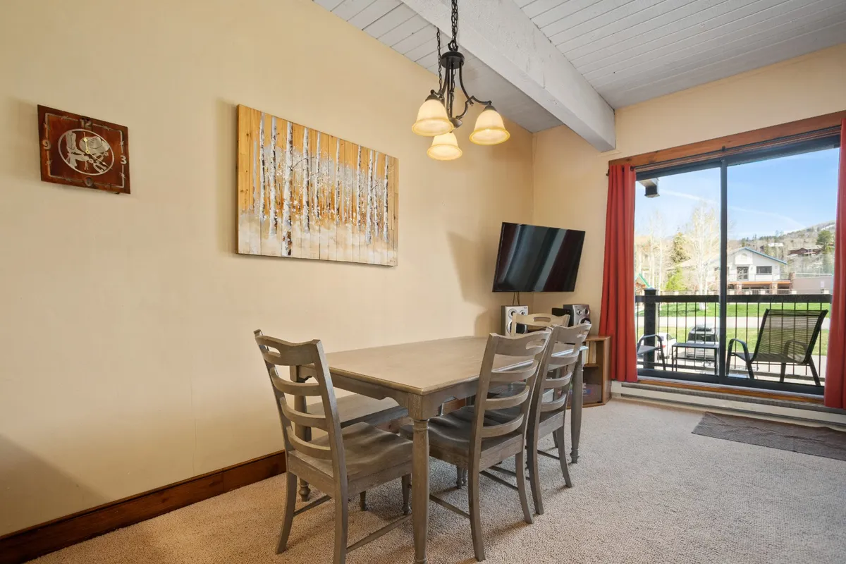 A bright dining area with a large table set for six, contemporary artwork on the wall, and a large window offering stunning views of the outdoors. The setting feels inviting, perfect for shared meals and memorable conversations.