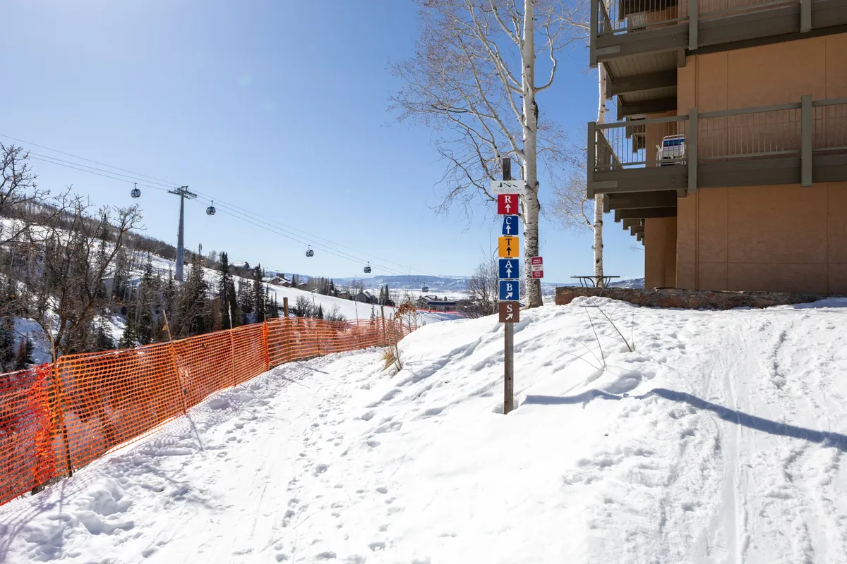 A snow-covered ski slope with clear signage and a nearby building structure, inviting skiers to embark on their journey. The scene is active and welcoming, underscoring the proximity of the accommodations to the slopes.